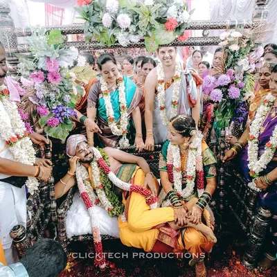 A fun and candid moment from a South Indian wedding ceremony, where the groom playfully rests on a swing while surrounded by laughing family and friends.
