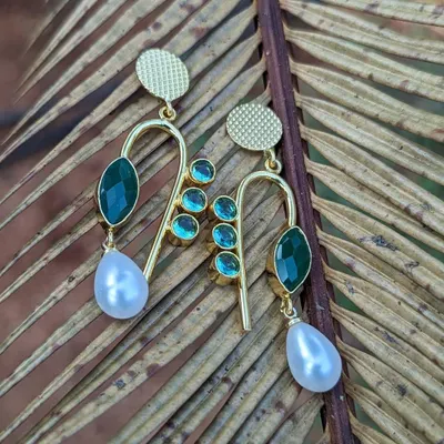 Add a pop of green to your look with these stunning brass earrings. The design features green stones and a delicate pearl drop, making them perfect for both western and Indian wear.
