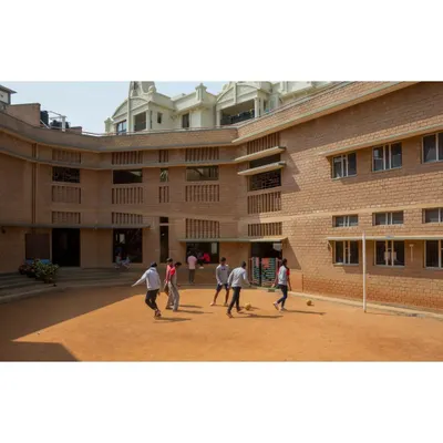 The shaded central courtyard of Buddhi School in Bengaluru, a vibrant hub for outdoor activities and play. The building's C-shaped plan was designed to create this protected space, using the structure itself to shield children from the harsh sun.