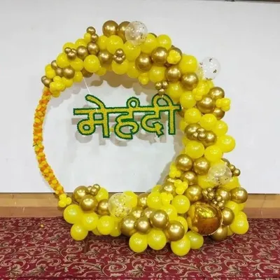 A bright and cheerful balloon decoration for a Mehendi ceremony. This circular arch is made with yellow and gold balloons and features a "मेहंदी" sign in the middle, creating a festive photo backdrop.
