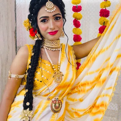 A perfect Haldi look with a yellow and white tie-dye saree. The makeup is bright and fresh, with a bold red lip and glowing skin, paired with a long traditional braid.