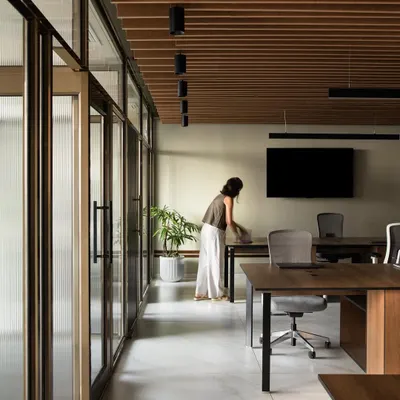 This wide shot of the office shows an open and airy workspace defined by a wooden slatted ceiling and glass partitions. The layout is designed for flexibility, allowing for easy movement and communication between different zones while maintaining a clean, uncluttered aesthetic.