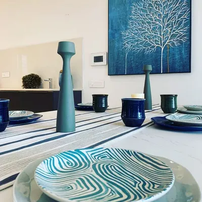 A close-up of a dining table setting, where patterned ceramic plates and accessories in shades of blue and teal complement a piece of abstract blue art on the wall. This shows our focus on curating a cohesive aesthetic down to the smallest detail.