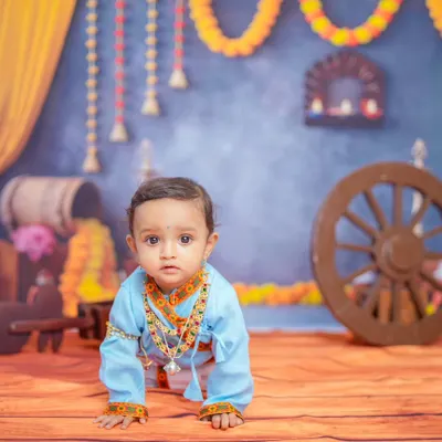 This crawling pose captures the baby's curiosity within the vibrant Krishna-themed set. The entire scene, from the marigold garlands to the wooden props, is carefully arranged for a complete look.