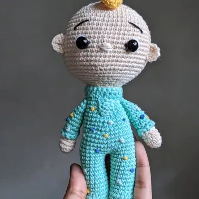 A handmade crochet doll of JJ from Cocomelon, held in my hand. He's wearing his signature blue pajamas with little yellow stars.