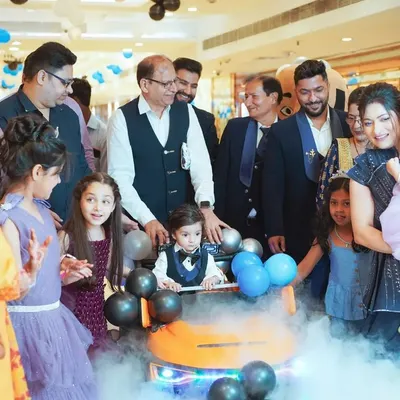The grand entrance is a moment of pure excitement. Here, the birthday boy makes his way through a cloud of smoke in his toy car, surrounded by cheering family and friends at his first birthday party.