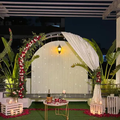 This is the complete romantic terrace setup at night. A floral arch is illuminated by fairy lights, with a candlelit table for two set for a private dinner.