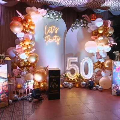 A full view of a 'Fabulous Fifty' birthday setup, combining a balloon arch, neon sign, marquee numbers, and personalized photo displays for a truly memorable celebration.
