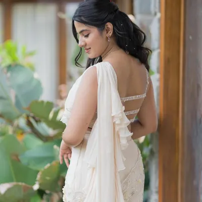 A beautiful back shot of a client in a white ruffled saree, her hair in soft waves, embodying effortless grace.