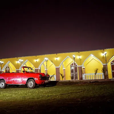 Our vintage red convertible parked in front of the lit-up yellow arched building at night. This setup is perfect for creating a dramatic, movie-like scene for your pre-wedding or commercial shoot.