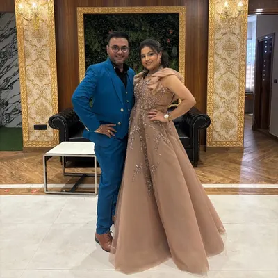 A happy couple ready for a celebration. She is wearing an elegant beige gown with delicate shoulder details, a perfect example of the sophisticated party wear available in our pre-owned collection.