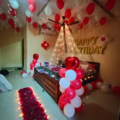 A full romantic birthday surprise room decoration, featuring a canopy bed with fairy lights, ceiling balloons, and a rose petal walkway.