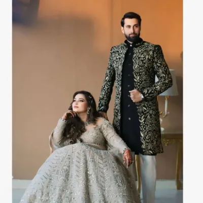 A stunning couple's portrait. The groom wears our black velvet Indo-Western sherwani with intricate all-over golden embroidery, paired with classic white trousers for a look of pure opulence.
