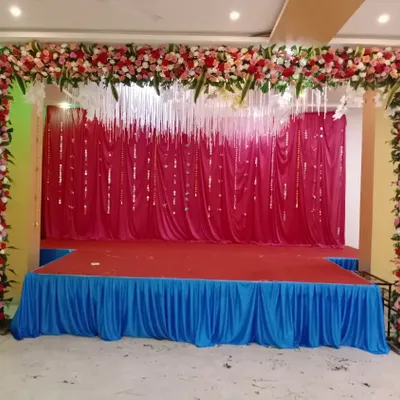 This is a versatile stage setup suitable for many events. It features a full arch of red, pink, and white flowers with hanging white floral strings over a red curtain backdrop.