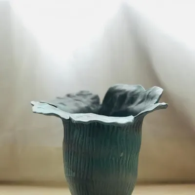 The Wild Petal Vase, a piece of functional sculpture. The hand-shaped rim mimics the organic form of a flower, and the textured, dark green glaze gives it a deep, earthy feel.