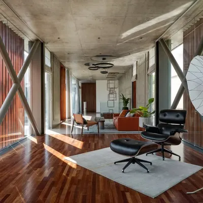 The interior of the Long House, where exposed structural cross-bracing and a concrete ceiling are paired with warm wood floors. This creates an industrial yet refined living space.