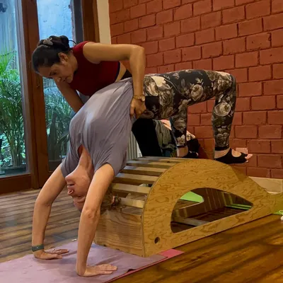 Train, Transform, Teach. An instructor provides a hands-on adjustment to a student practicing a backbend over a wooden prop. This is a glimpse into our 200-hour Yoga Teacher Training Course, where you get personalized guidance.