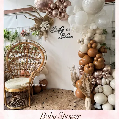 A soft and elegant 'Baby in Bloom' baby shower setup. The neutral-toned balloon arch, pampas grass, and wicker peacock chair create a warm and stylish vibe for the mom-to-be.