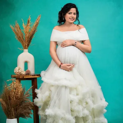 An absolute vision in white. This off-the-shoulder gown with a cloud-like ruffled skirt is a dream come true for a Pinterest-worthy maternity shoot. It's pure elegance and romance.