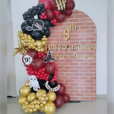 Welcome to Hogwarts! This magical Harry Potter themed backdrop is perfect for a 9th birthday. It features a brick wall arch reminiscent of Platform 9 3/4, surrounded by an organic balloon garland in Gryffindor colors with themed cutouts like Hedwig and the Golden Snitch.