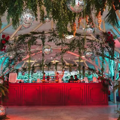 The vibrant red bar stands out against the lush greenery and hanging disco balls of our 'Jungle Disco' theme. This setup was designed to be the energetic heart of the reception party.