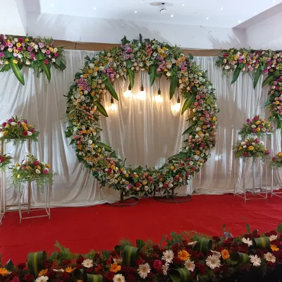 For this reception stage, we created a large circular floral wreath with mixed flowers and hanging bulbs. This modern floral backdrop design makes a big statement against the simple white drape background and red carpet, creating a focal point for the event.