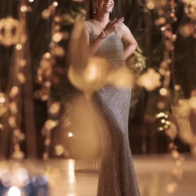 A client captured in a candid moment, glowing in her custom champagne sequin gown. The beautiful bokeh background highlights the dress's sparkle, perfect for any glamorous evening event.