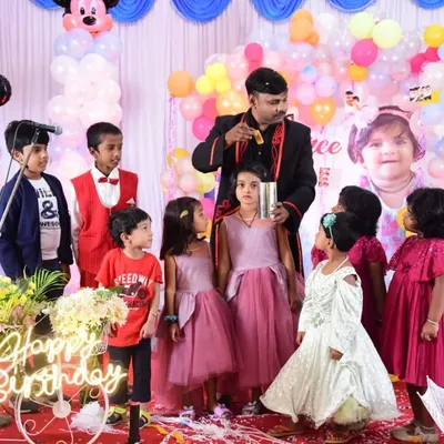 A full stage setup for a fantastic birthday celebration. Surrounded by an eager audience of kids, I’m performing a classic cup and ball trick. The colorful balloons and happy faces say it all.