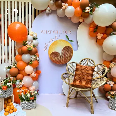 This "Little Cutie" gender reveal setup combines a playful theme with chic design. A custom backdrop, a stylish rattan chair, and a vibrant orange and white balloon arch create a stunning focal point for photos and fun.