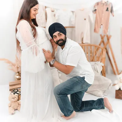 A joyful dad to be listens to the baby bump during a studio maternity shoot. The background is styled with neutral baby clothes, creating a warm and loving scene.