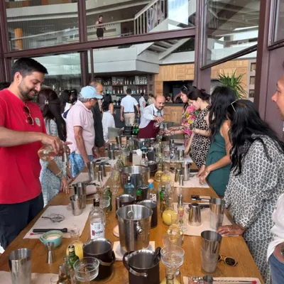A wide shot of our cocktail workshop in progress. Guests are gathered around a long table, each with their own shaker and ingredients, ready to learn the art of mixology from our experts.