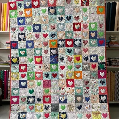 A heartwarming memory quilt made from a daughter's baby clothes. Each square features a tiny heart appliquéd from a different piece of clothing, creating a tapestry of childhood memories.