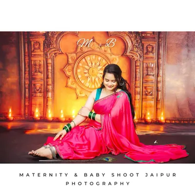 A beautiful full-length portrait of a woman in a bright pink saree, seated gracefully in a traditionally decorated studio. The warm lighting from the diyas creates a festive and serene atmosphere.