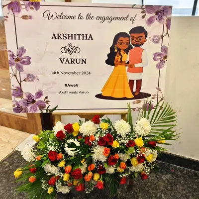 A charming and personal welcome sign for an engagement, featuring a custom caricature of the couple. The sign is beautifully presented on an easel with a fresh arrangement of colorful flowers.