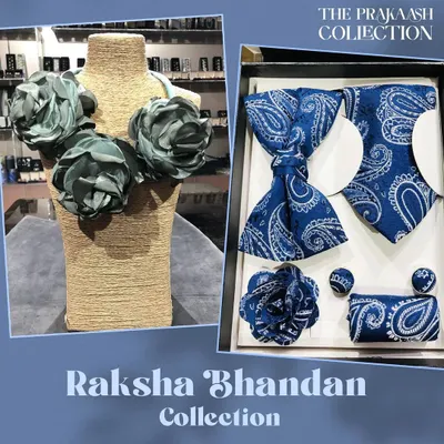 A perfect pairing for gifting, this set includes a men's accessory box with a blue paisley bow tie, tie, pocket square, and cufflinks. It is shown alongside a women's statement necklace made of soft, grey-blue fabric flowers.