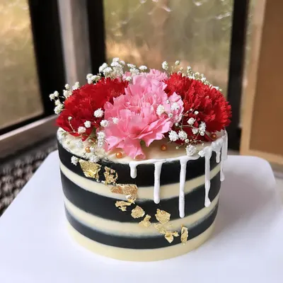 A striking black and white striped cake with a white chocolate drip, gold leaf, and a beautiful arrangement of fresh carnations. This design is modern, bold, and elegant.