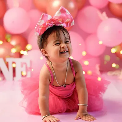 The pure, uncontainable joy of turning one! This little girl's infectious giggle is the centerpiece of her pink-themed first birthday photoshoot, surrounded by balloons and festive lights.