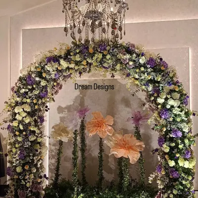 A perfect backdrop for a baby shower celebration. This beautiful floral arch, made with a mix of real and oversized paper flowers, sits under an elegant chandelier, creating a whimsical and sophisticated photo corner.