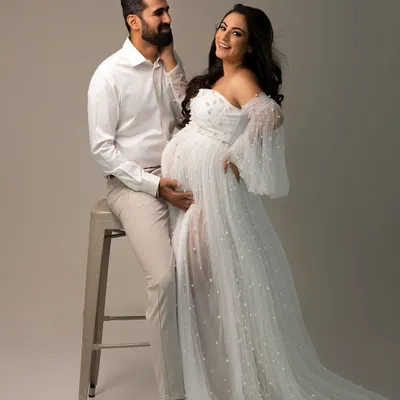 A joyful, candid moment during an elegant couple's maternity shoot. Her smile says it all, surrounded by the soft tulle of her beautiful gown.
