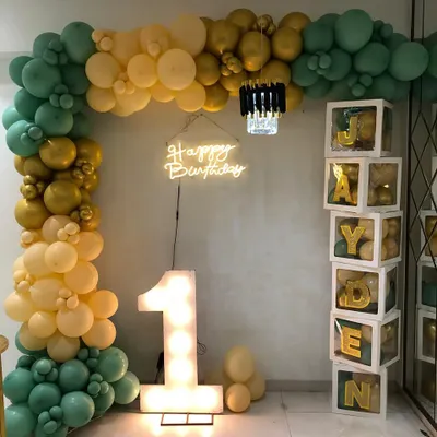 A stylish and modern first birthday for Jayden. This setup features a beautiful balloon arch in sage green, gold, and cream, a light-up number '1', a neon sign, and custom blocks spelling out his name.