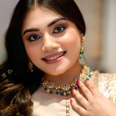 A close-up beauty shot of a model for a jewelry collaboration, her bright smile highlighting a stunning emerald and pearl necklace from Kay Jewellers.