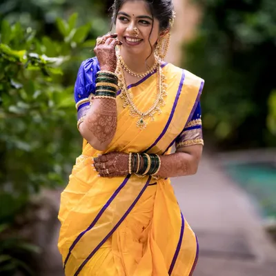 A joyful Maharashtrian bride in her vibrant yellow and blue Nauvari saree. Her makeup is soft and natural, complementing the traditional attire perfectly.