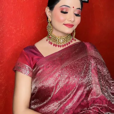 A complete traditional look featuring a beautiful maroon silk saree. The makeup includes shimmery red eyeshadow, a flawless base, and a matching red lip, perfect for a wedding reception or festive occasion.