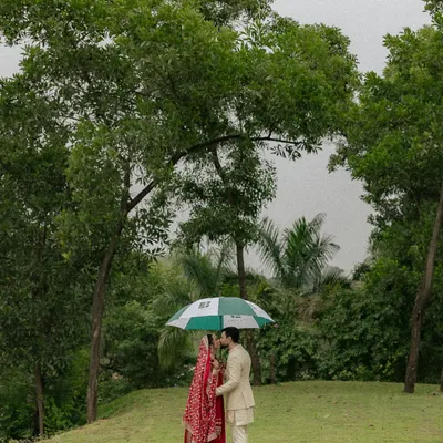 A quiet moment under an umbrella amidst the greenery of Oleander Farms. This shot captures the intimacy and romance of a monsoon wedding, with the couple lost in their own world.
