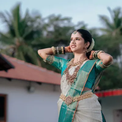 A stunning portrait of a South Indian bride in a traditional white and teal silk saree, capturing her elegance and anticipation on her wedding day.