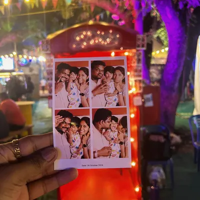 This is the prize at the end of the fun. A close-up of a classic four-shot photo strip, held up against the backdrop of the event. These instant prints are a tangible reminder of a great time with family and friends.