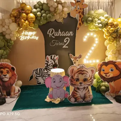A grand jungle safari theme for Ruhaan's 2nd birthday. This stage decoration features large, cute animal cutouts, a marquee number '2', and a lush balloon arch in shades of green, white, and gold, creating an immersive wildlife experience.