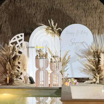 This is the essence of boho chic. A poolside birthday setup featuring layered white arch backdrops, dried pampas grass, and our signature slatted plinths for a look that's both rustic and refined.