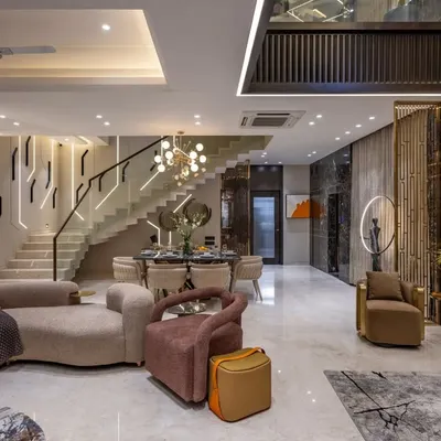 This duplex living room combines dramatic lighting on the staircase with plush, curved sofas to create a dynamic yet inviting atmosphere. We used dark marble and metallic accents to add a layer of opulence and connect the different zones.