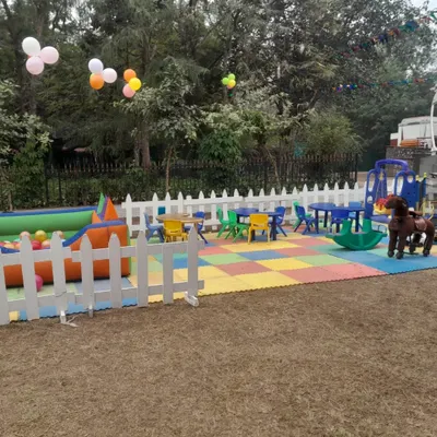 A complete kids' play zone set up outdoors, featuring soft interlocking floor mats, a white picket fence for safety, a ball pool, ride-on toys, and kid-sized tables and chairs.
